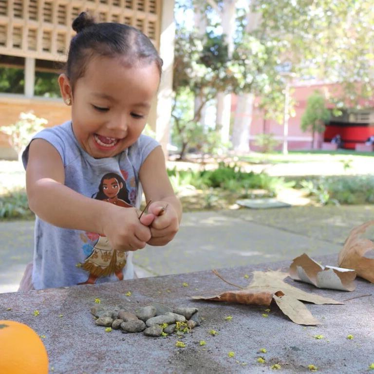 Small child at UC Riverside campus playing with leaves and rocks